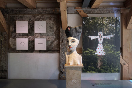 FERNES RAUSCHEN, NAHES LEUCHTEN | Die Gärten des Jochen Bach in Plinz. Rechts: Skulptur „Ätna“, dahinter eine fotografische Abbildung des letztendlichen Engels, geschaffen von Jochen Bach, der an seinem Mühlengehöft in Plinz den Garten der Stille geaschaffen hat. Links: 4 Texte von Eugen Gomringer in Blockhängung aus dem Mappenwerk "das geheimnis im roten" im Verlag Bärbel Müller des KUNSTHAUS MÜLLER (1995, Auflage 13 Exemplare, Offset-Druck) Foto: Wolfgang Grau FERNES RAUSCHEN, NAHES LEUCHTEN Die Gärten des Jochen Bach in Plinz